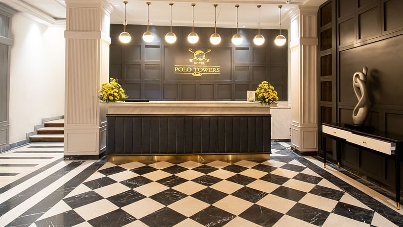 A grand reception area at Hotel Polo Towers, featuring a checkered floor, a luxurious chandelier, and a stylish reception desk.